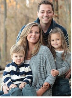 a man, woman and two children posing for a photo in front of some trees