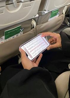 a person sitting on an airplane holding a cell phone and looking at the screen with both hands