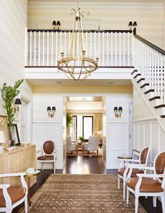 a living room filled with furniture and a chandelier hanging from the top of a stair case