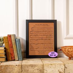 there is a framed sheet music print on the shelf next to some books and a bowl