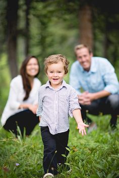 a little boy walking through the grass with his parents