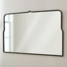 a mirror hanging on the wall in front of a window with white walls and windowsill