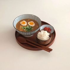 a bowl of soup and chopsticks on a wooden tray with an egg in it