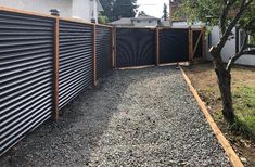 a fence that is next to a tree and some gravel in front of a house