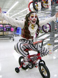 a woman dressed as a clown riding a bike in a store with her arms outstretched