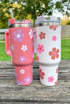 two travel mugs sitting next to each other on a picnic table in the grass