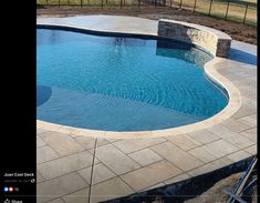 a swimming pool surrounded by a stone patio and fenced in area with an outdoor fire pit