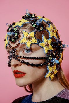 a woman wearing beaded headpieces and beads on her face, against a pink background