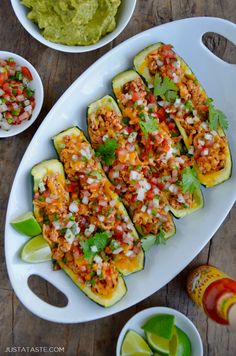 stuffed zucchini boats with salsa and guacamole in the background on a white platter