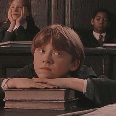 a young boy sitting at a desk with his hands on his chin and two other children in the background