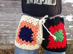 a woman is holding two crocheted bags in front of a wooden fence and grass