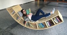 a woman laying on top of a wooden boat shaped chair with bookshelves attached to it