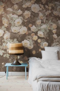 a bedroom with floral wallpaper and a bed in the foreground, next to a lamp on a table