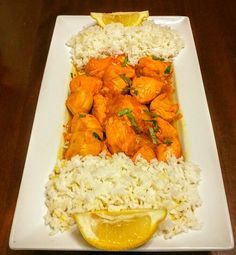 a white plate topped with rice and chicken next to a slice of lemon on top of a wooden table