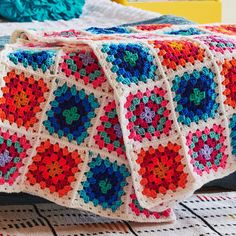 a colorful crocheted blanket on top of a bed next to pillows and blankets