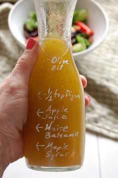 a person holding up a glass bottle filled with liquid next to a bowl of salad