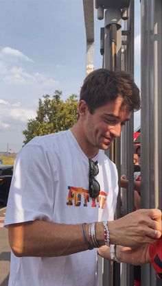 a man in a white shirt is looking at his cell phone while standing next to a pole