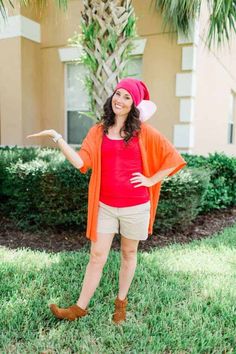 a woman standing in the grass with her arms out and wearing an orange cardigan