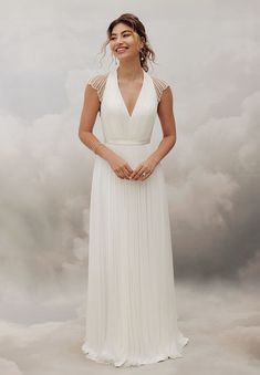 a woman wearing a white dress standing in front of a cloud filled sky with her hands on her hips