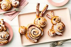 cinnamon buns with icing on a plate next to silverware and utensils