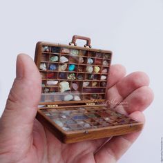 a hand holding a small wooden box filled with lots of different items in it's palm