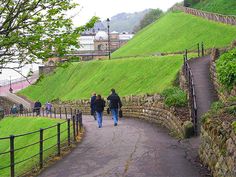 two people walking down a path next to a lush green hillside