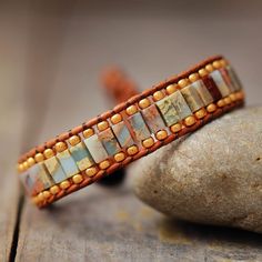 a beaded bracelet sitting on top of a rock next to a small piece of wood