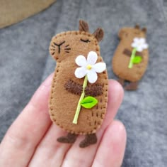 a hand holding a tiny felt animal with a flower in it's mouth and another small one behind it