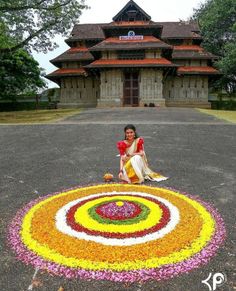 a woman sitting on the ground in front of a building with flowers all over it