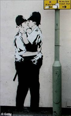 a couple kissing in front of a wall with a street sign next to it,