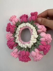 a hand holding a pink and white crocheted flower brooch with green leaves