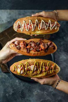 two people holding hot dogs in buns with toppings