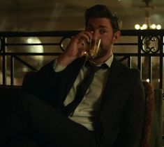 a man sitting in a chair drinking from a wine glass while wearing a suit and tie