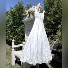 a white dress hanging on a clothes rack in front of some bushes and trees,