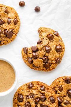 three cookies with chocolate chips and a cup of coffee on the table next to them