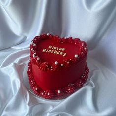 a red heart shaped birthday cake sitting on top of a white cloth