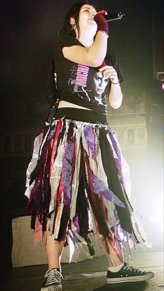 a woman standing on top of a stage wearing a skirt and holding a microphone in her hand