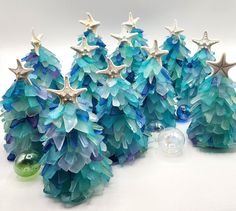 three small trees made out of blue and green glass beads with silver stars on them