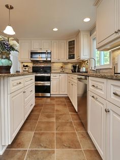 a large kitchen with white cabinets and tile flooring, along with stainless steel appliances