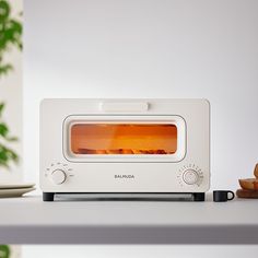 a white toaster oven sitting on top of a counter next to a plate with bread