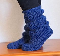 a pair of blue crocheted boots sitting on top of a wooden table next to a person's legs