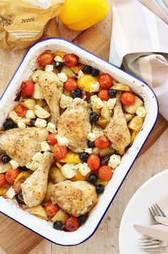 a casserole dish with chicken, tomatoes and olives on a wooden table