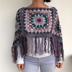 a woman is wearing a crocheted shawl with tassels on it