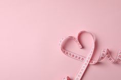 a heart shaped measuring tape with the word love spelled in it on a pink background