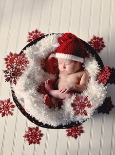 a baby wearing a santa hat laying in a bowl with snowflakes around it