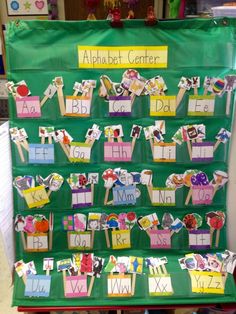 a green bulletin board with letters and pictures on it in front of a classroom desk