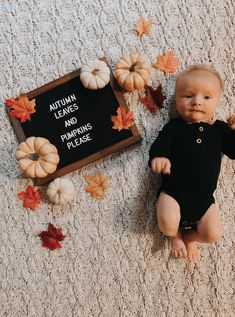 a baby sitting on the floor next to a sign that says autumn leaves and pumpkins please