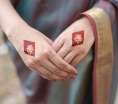 two hands with red and gold designs on them, one holding the other's hand