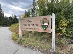 a wooden sign sitting on the side of a road next to some bushes and trees