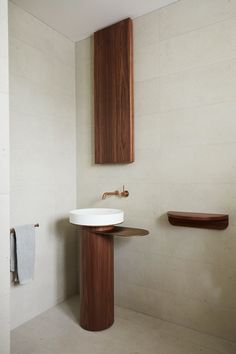 a white sink sitting under a bathroom mirror next to a wooden shelf and towel dispenser